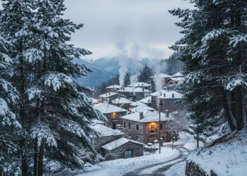 Χιονισμένο παραδοσιακό χωριό στην ορεινή Ελλάδα με πέτρινα σπίτια και τζάκια που καπνίζουν