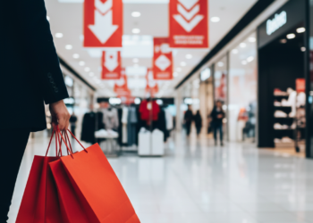 Κόκκινες τσάντες αγορών και ταμπέλες με το σύμβολο του ποσοστού εκπτώσεων μπροστά από βιτρίνα